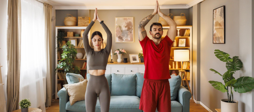 Couple practicing yoga together at home in a living room, promoting physical fitness and a healthy lifestyle for fertility.